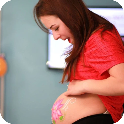 Pregnant woman smiling at her floral belly painting – intimate moment.