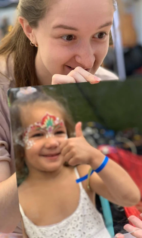 BloomART face painter smiling with happy girl showing thumbs up after face painting