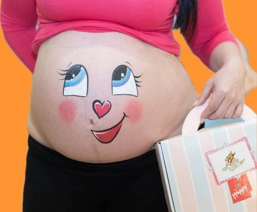 Smiling cartoon face painted on pregnant belly – cheerful and playful design.