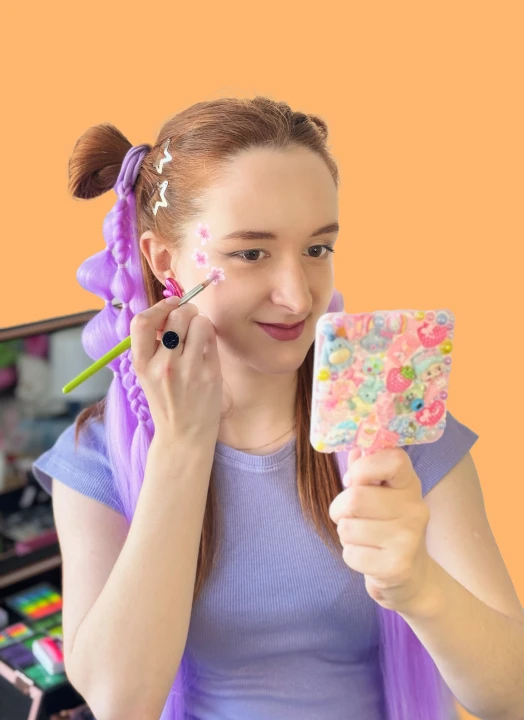 Face painting artist applying stars to her cheek using a mirror