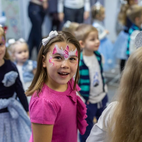 Girl with butterfly face paint in a pink dress smiling at a party